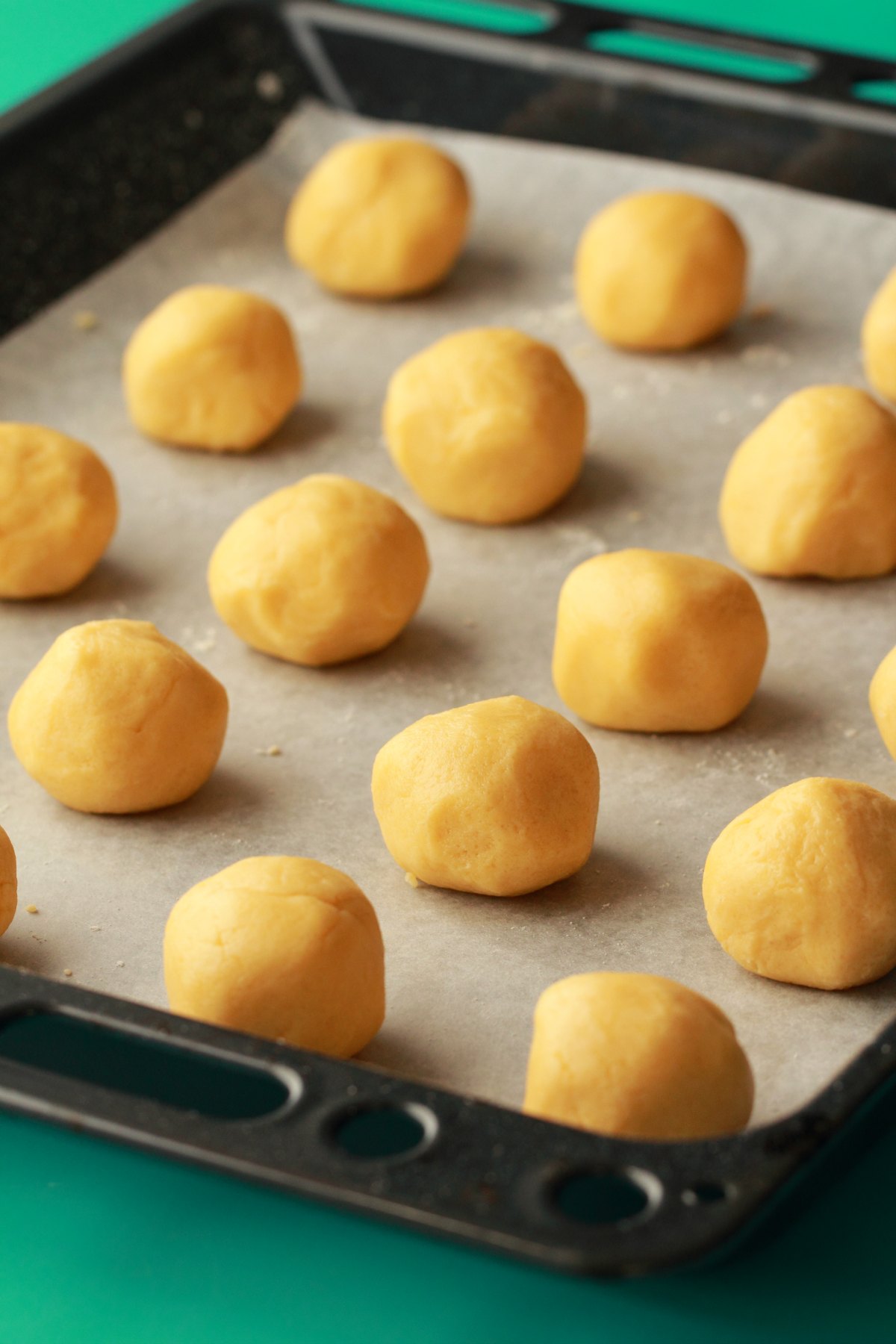 Balls of cookie dough lined up on a parchment lined baking tray. 
