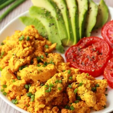 Vegan tofu scramble with sliced avocado and fried tomatoes on a white plate.