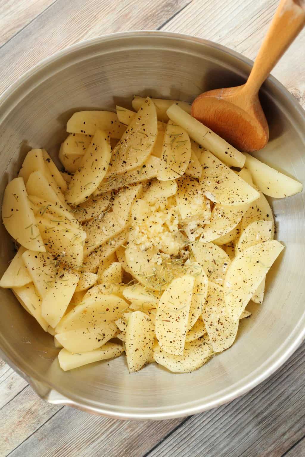 Sliced potatoes and spices in a mixing bowl getting ready to make baked potato fries.