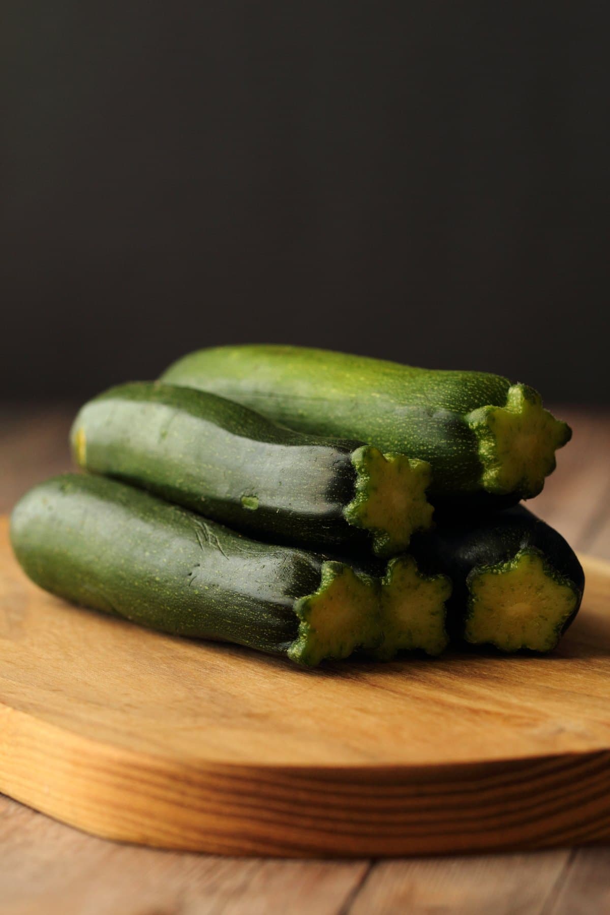 Zucchinis stacked up on a wooden board. 