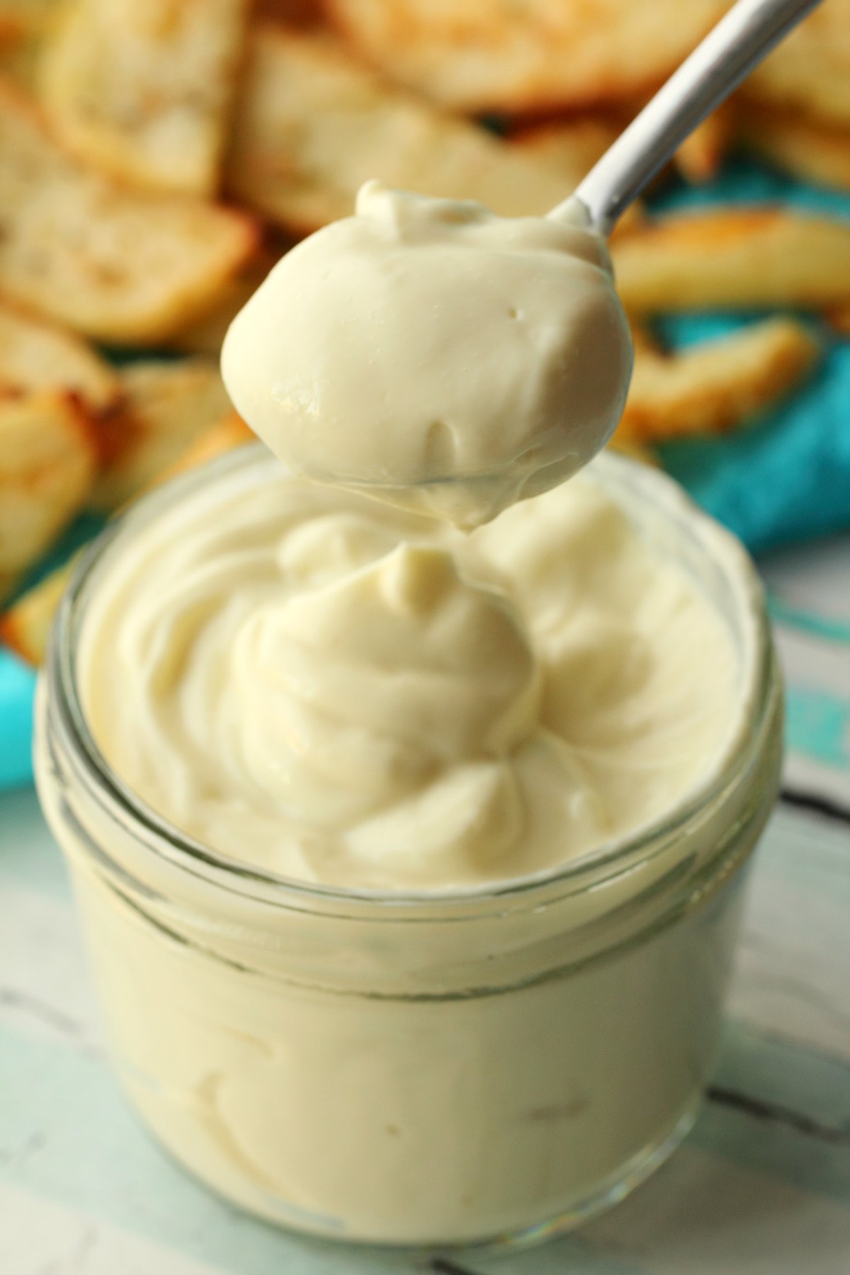 A spoonful of vegan mayo above a glass jar of mayo. 