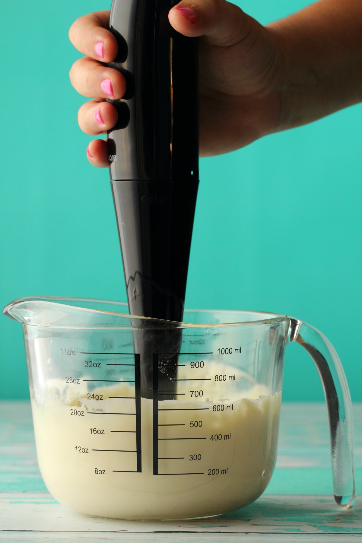 Vegan mayo being blended in a glass measuring jug with an immersion blender. 