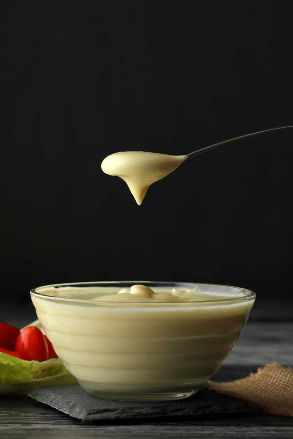 Vegan Mayonnaise in a glass bowl with a spoonful of mayo above it. 