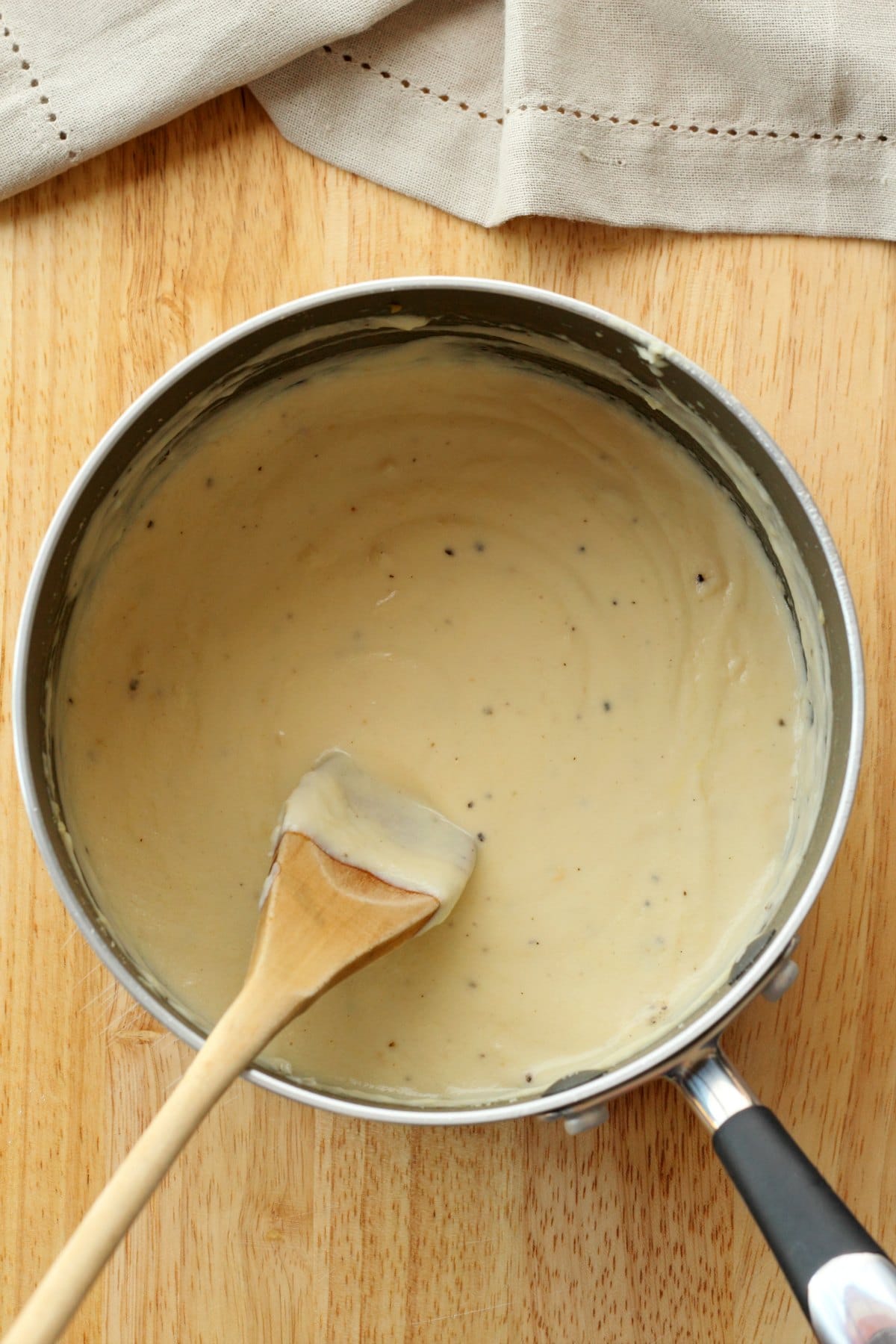White sauce in a saucepan with a wooden spoon. 