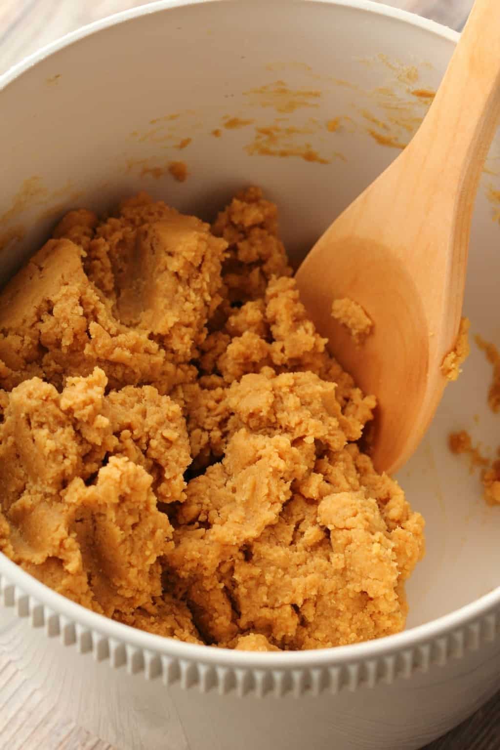 Batter for Vegan Peanut Butter Chocolate Chip Cookies in a white mixing bowl with a wooden spoon. 