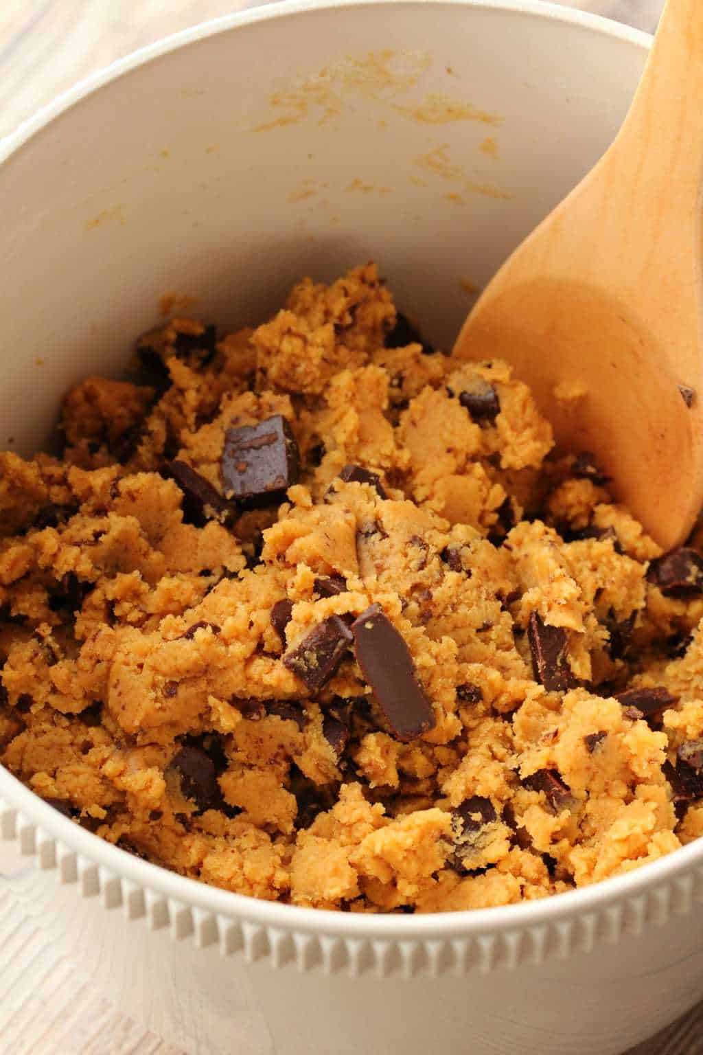 Mixing up the cookie dough for Vegan Peanut Butter Chocolate Chip Cookies in a white mixing bowl with a wooden spoon. 