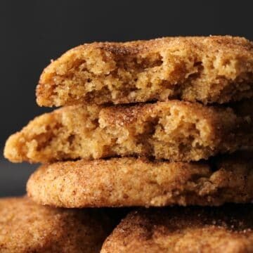 Vegan snickerdoodles in a stack with the top cookie broken in half.