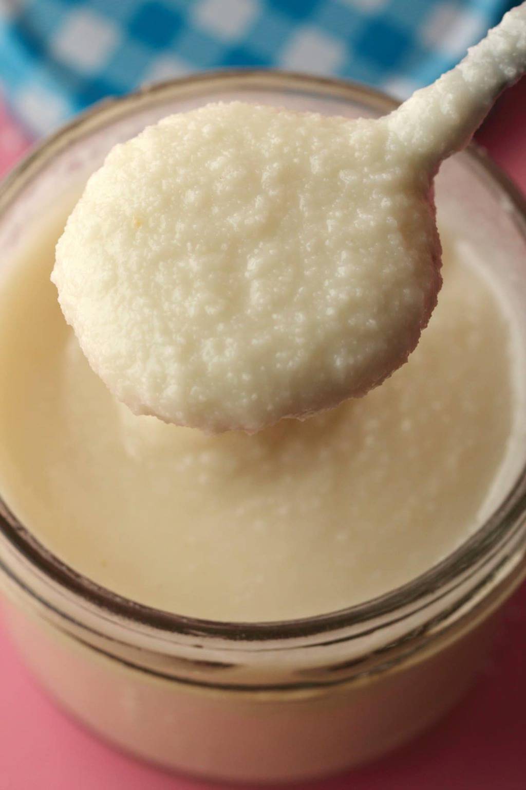 Coconut butter in a glass jar with a spoonful lifting out showing the texture. 
