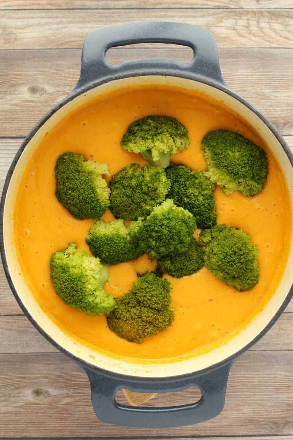 Adding broccoli florets to soup in a large pot. 