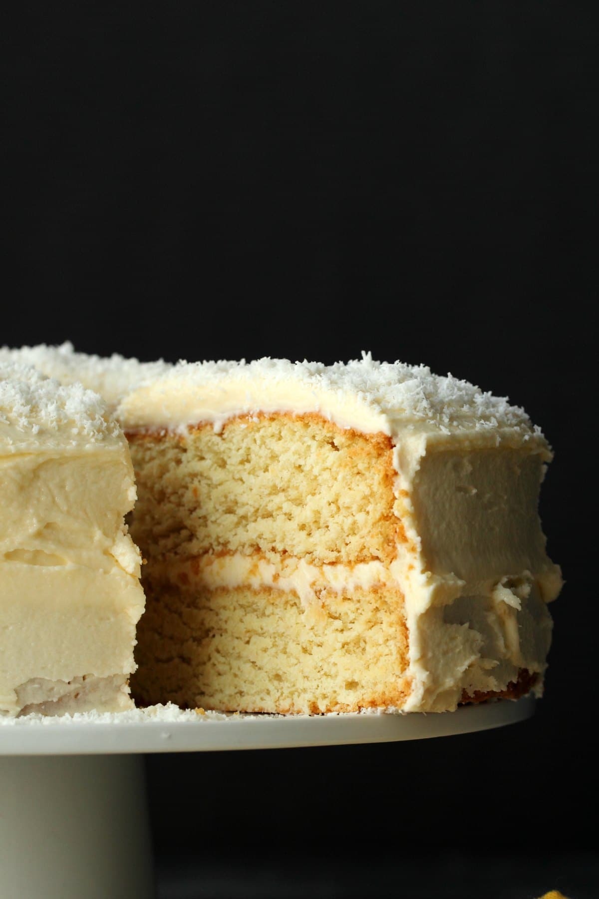 Coconut cake on a white cake stand with one slice cut and ready to be served. 