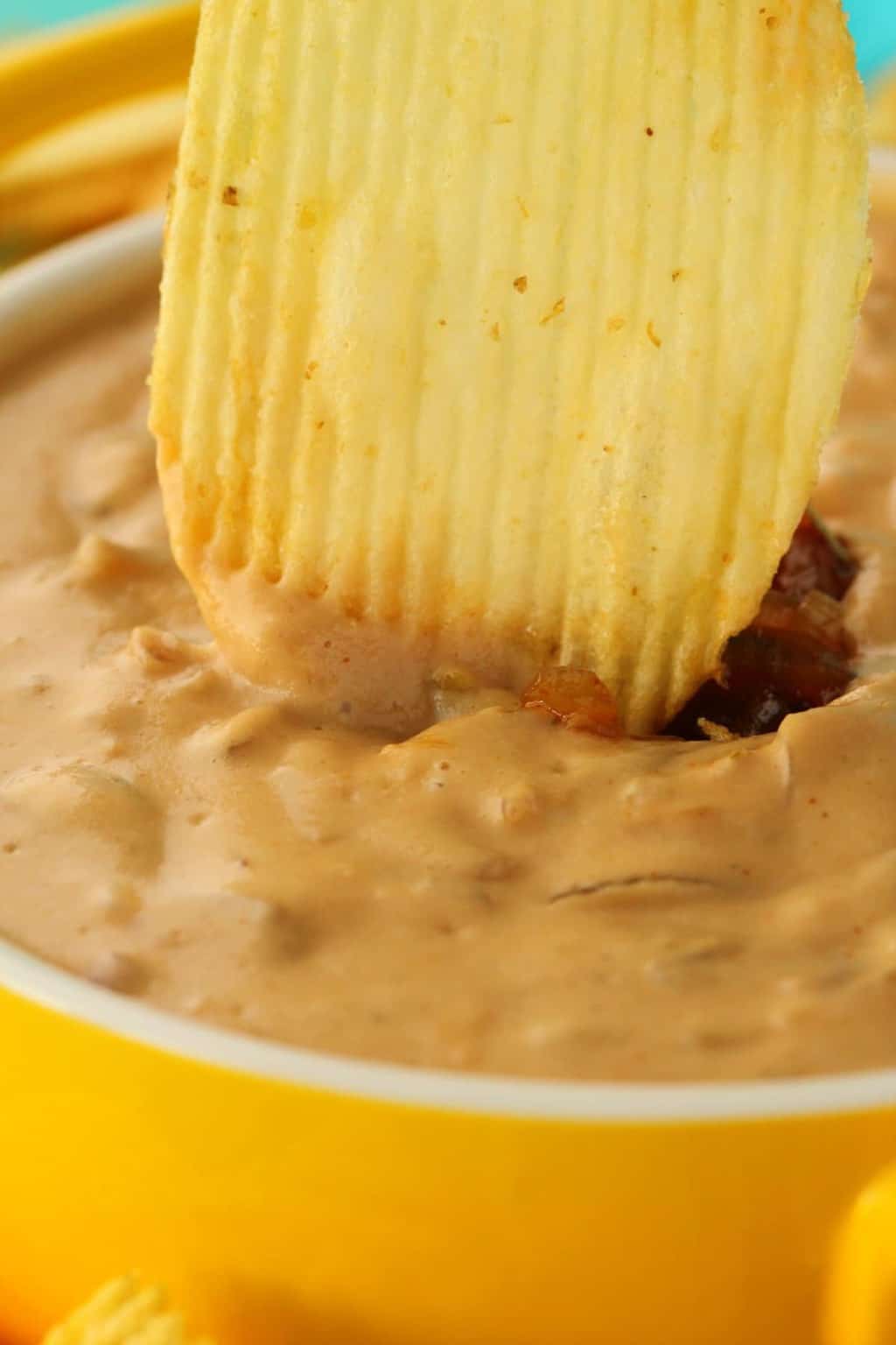 A chip dipping into a bowl of vegan onion dip. 