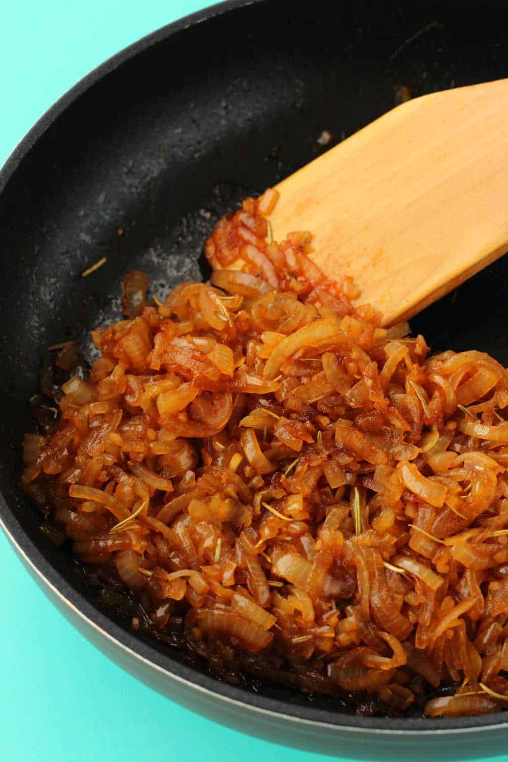 Caramelized onions in a frying pan with a wooden spoon. 