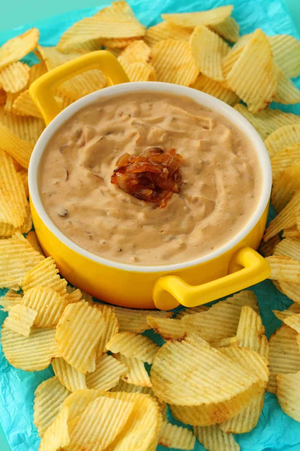 Vegan Onion Dip in a yellow and white serving dish surrounded by chips. 