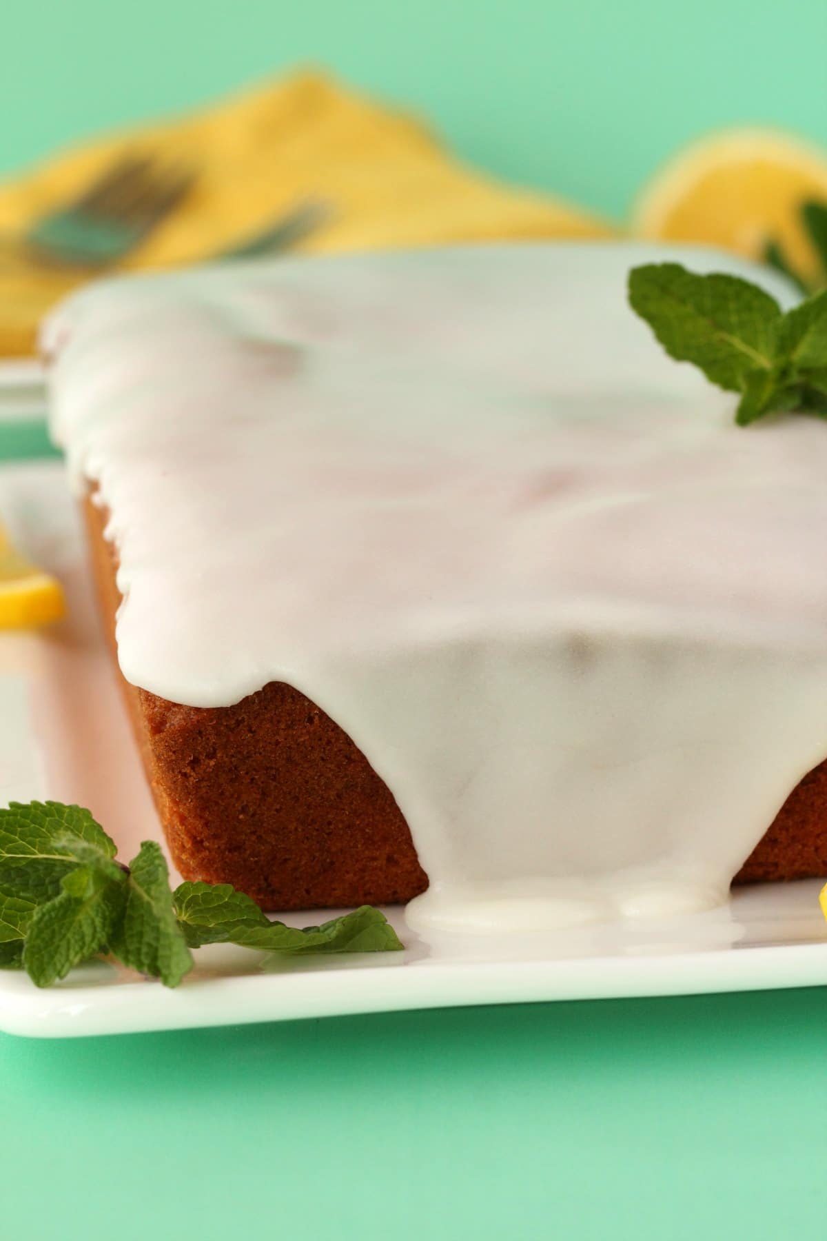 Pound cake topped with lemon glaze, on a white plate with mint leaves and lemon slices. 