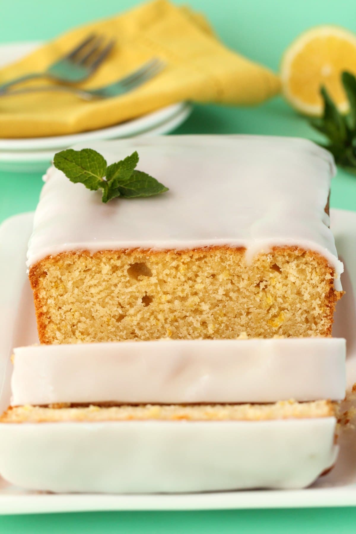 Vegan lemon loaf cake topped with lemon glaze on a white plate. 