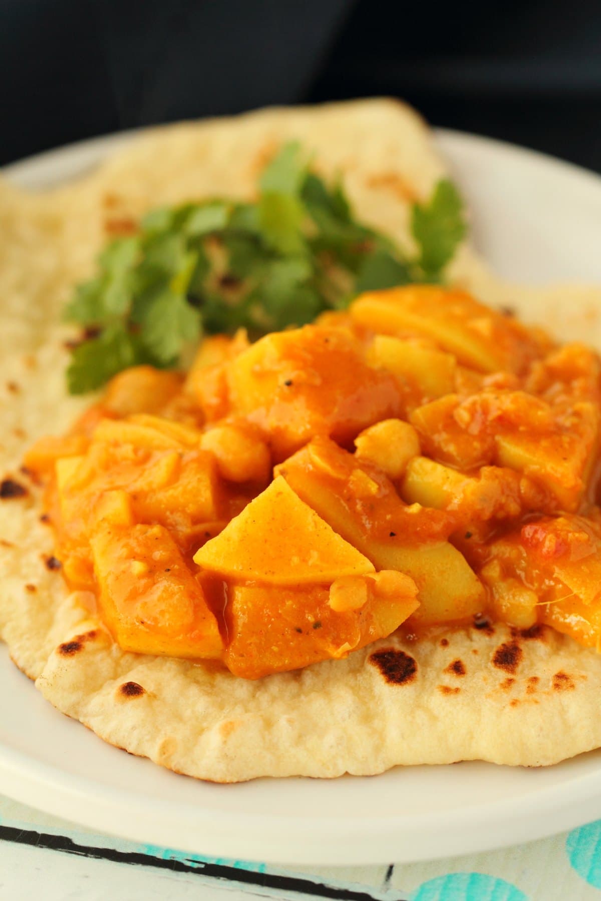 Vegan naan topped with vegan potato curry on a white plate. 