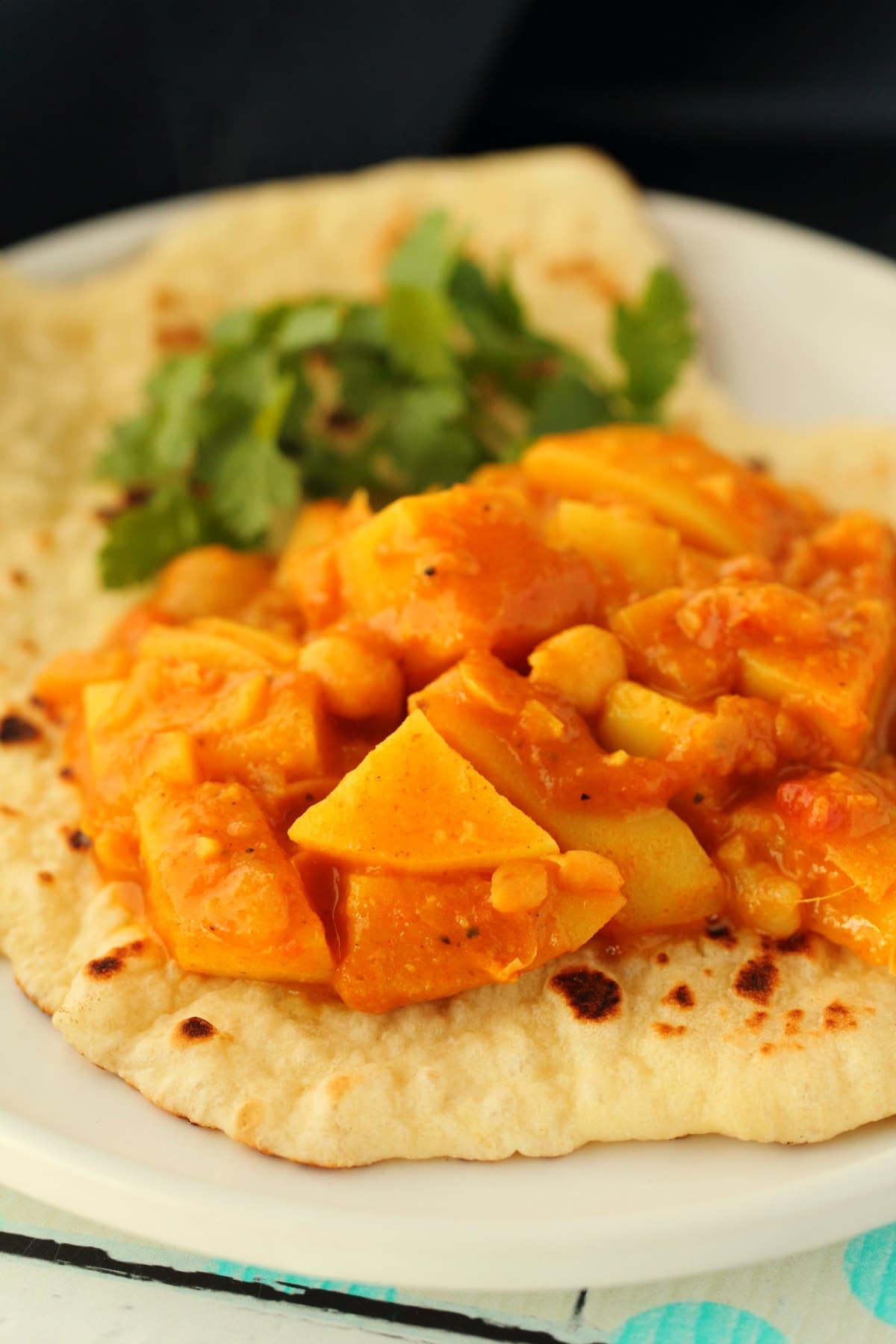 Vegan potato curry with vegan naan on a white plate. 