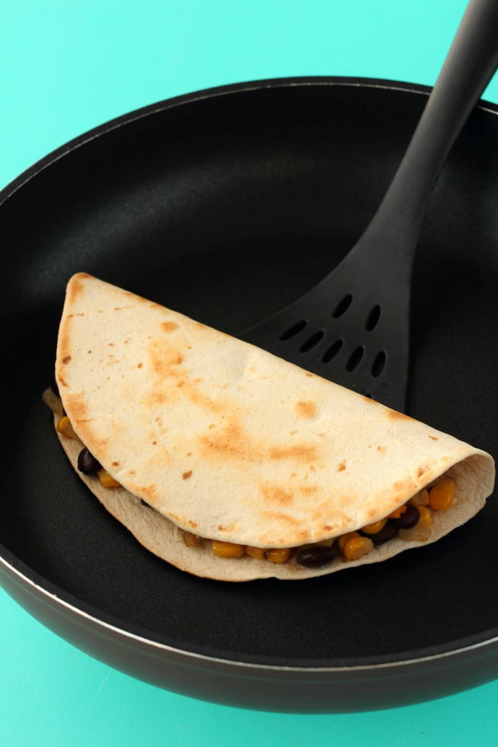 A vegan quesadilla in a frying pan with a spatula. 