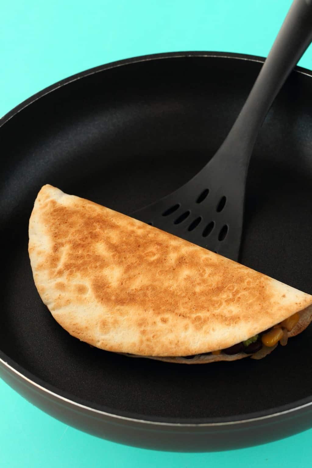 A cooked vegan quesadilla in a frying pan with a spatula. 