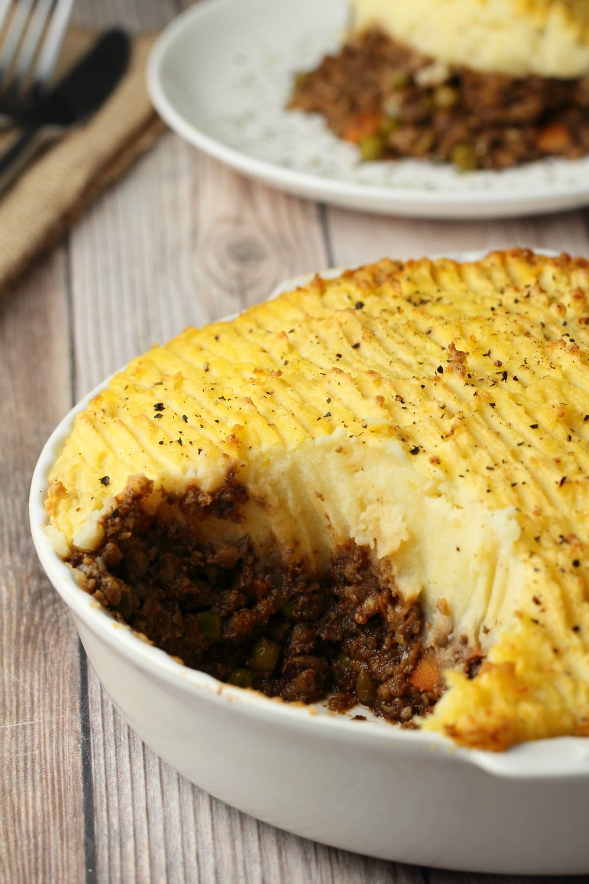 Vegan shepherd's pie in a white pie dish, with a piece cut out. 