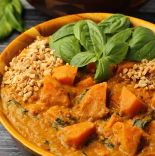 Vegan sweet potato curry with fresh basil in a wooden bowl.