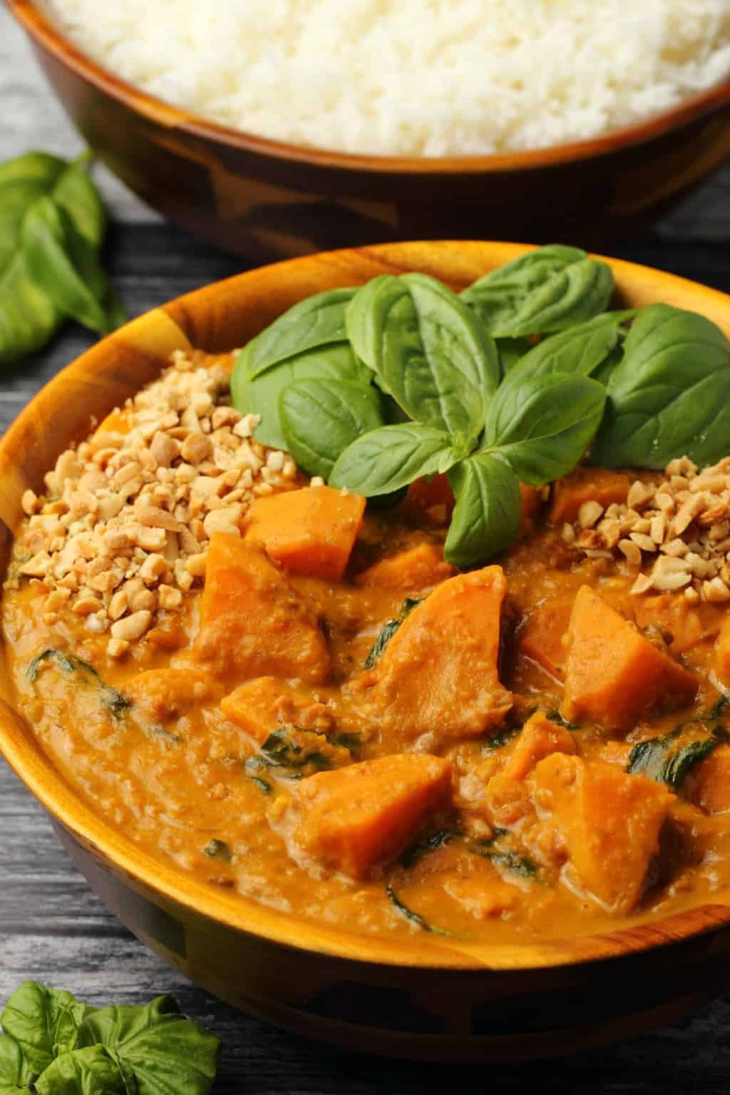 Vegan Sweet Potato Curry topped with fresh basil leaves and crushed peanuts in a wooden bowl. 