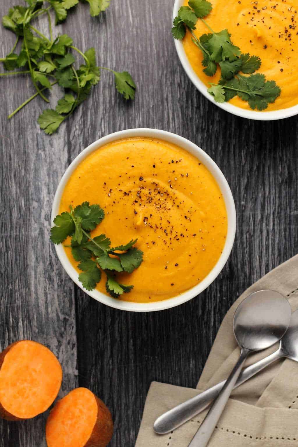 Vegan Sweet Potato Soup topped with black pepper and fresh cilantro in white bowls. 