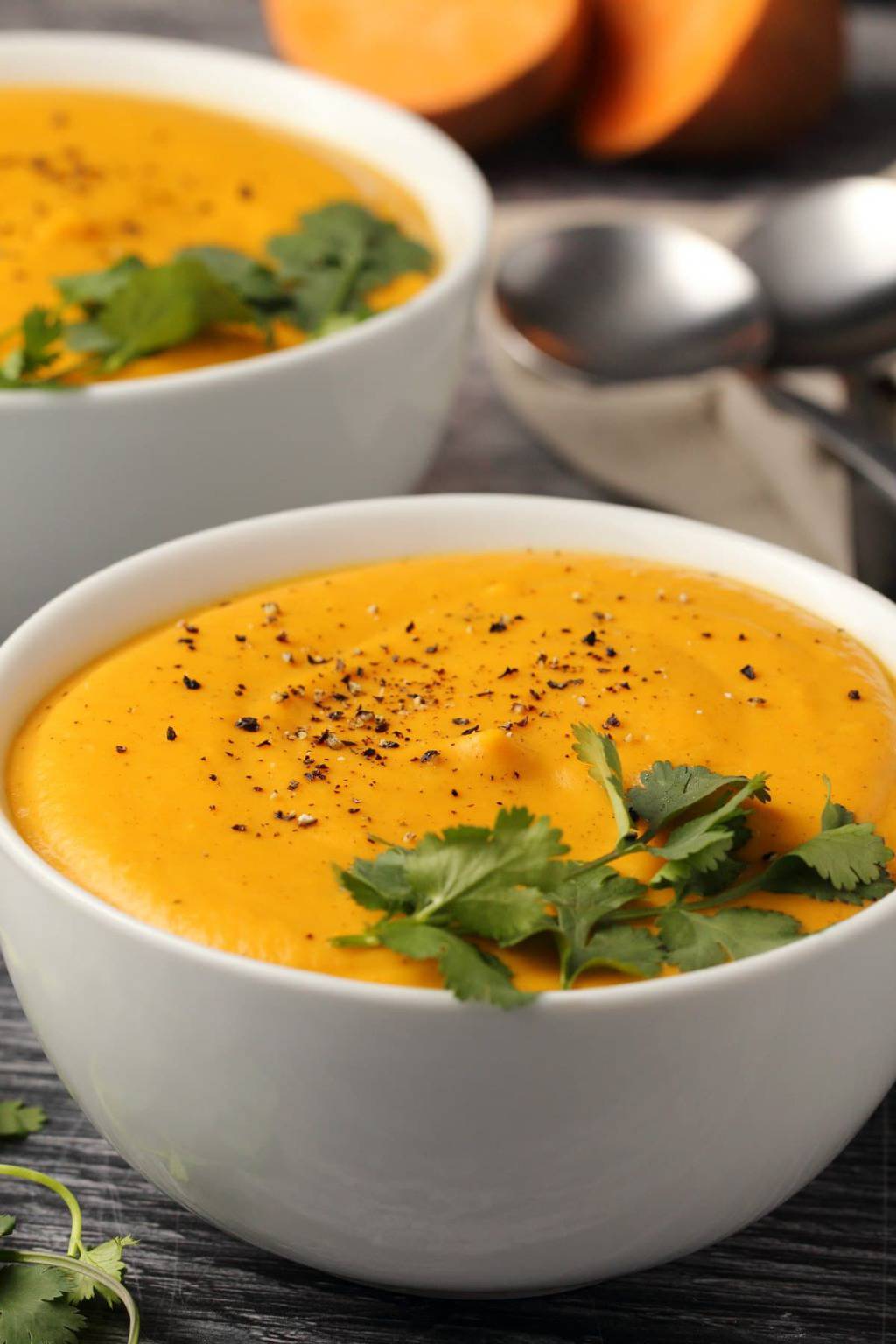 Vegan sweet potato soup topped with black pepper and fresh cilantro in white bowls. 