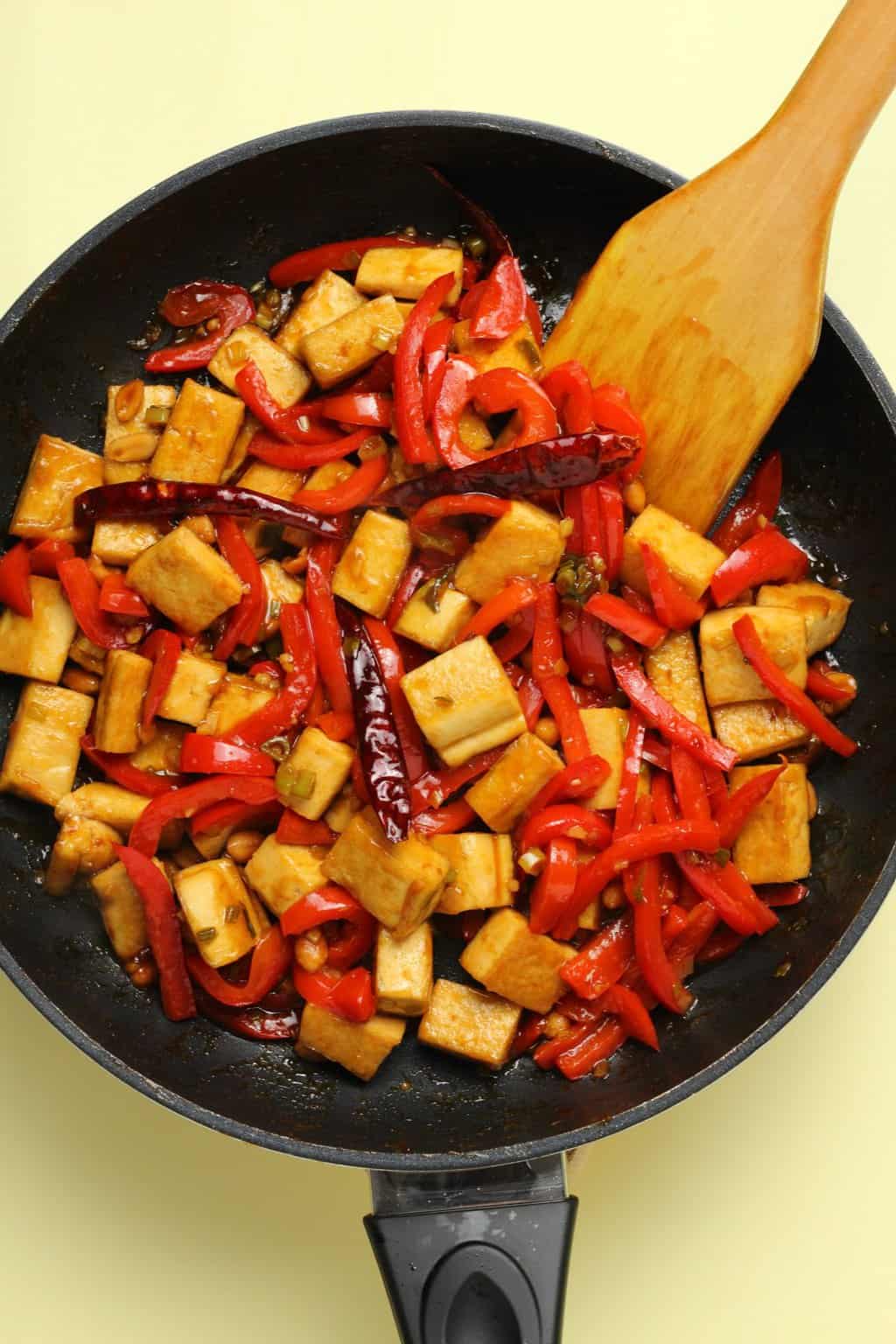 Kung pao tofu in a frying pan with a wooden spatula.