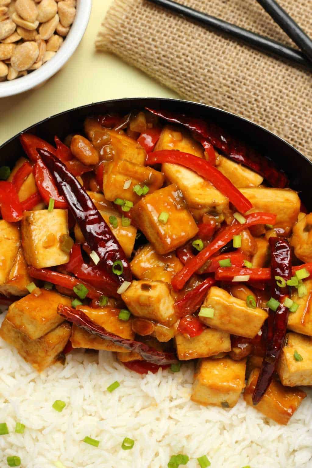 Kung pao tofu served in a wok with basmati rice and topped with chopped spring onions.