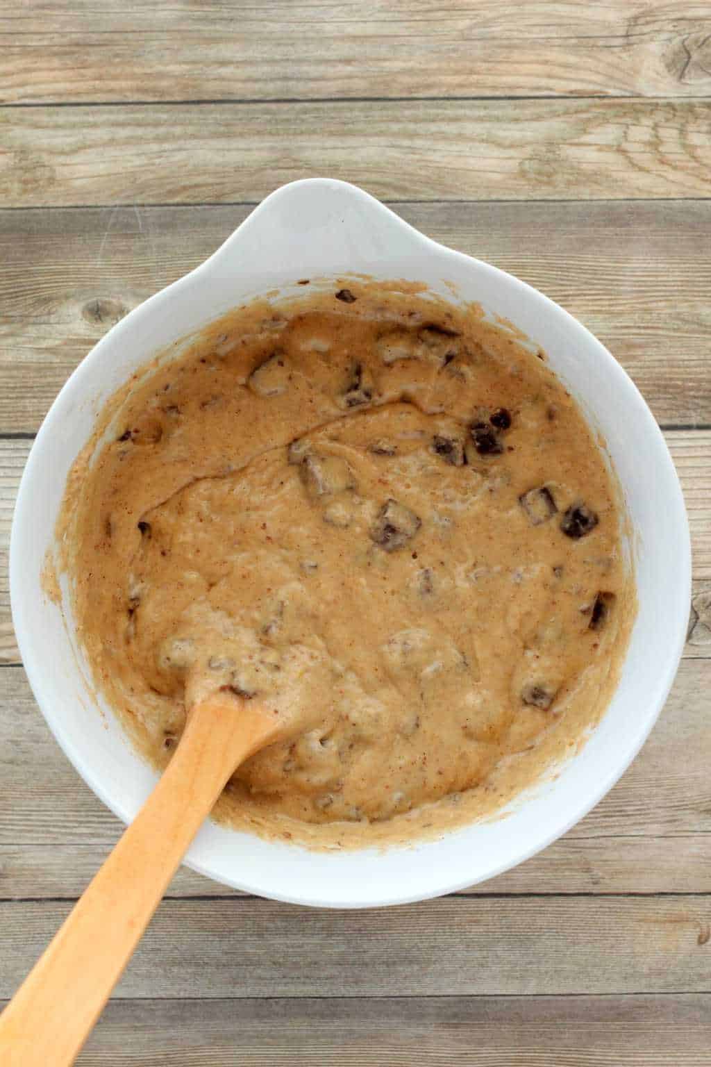 Batter for vegan banana chocolate chip muffins in a white mixing bowl with a wooden spoon. 