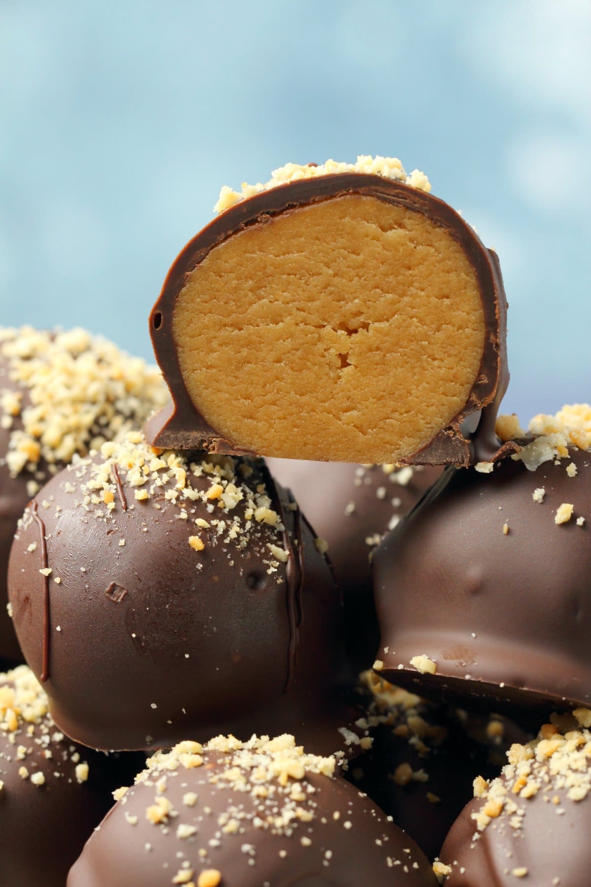 Vegan peanut butter balls stacked up with the one on top cut in half to show the center. 