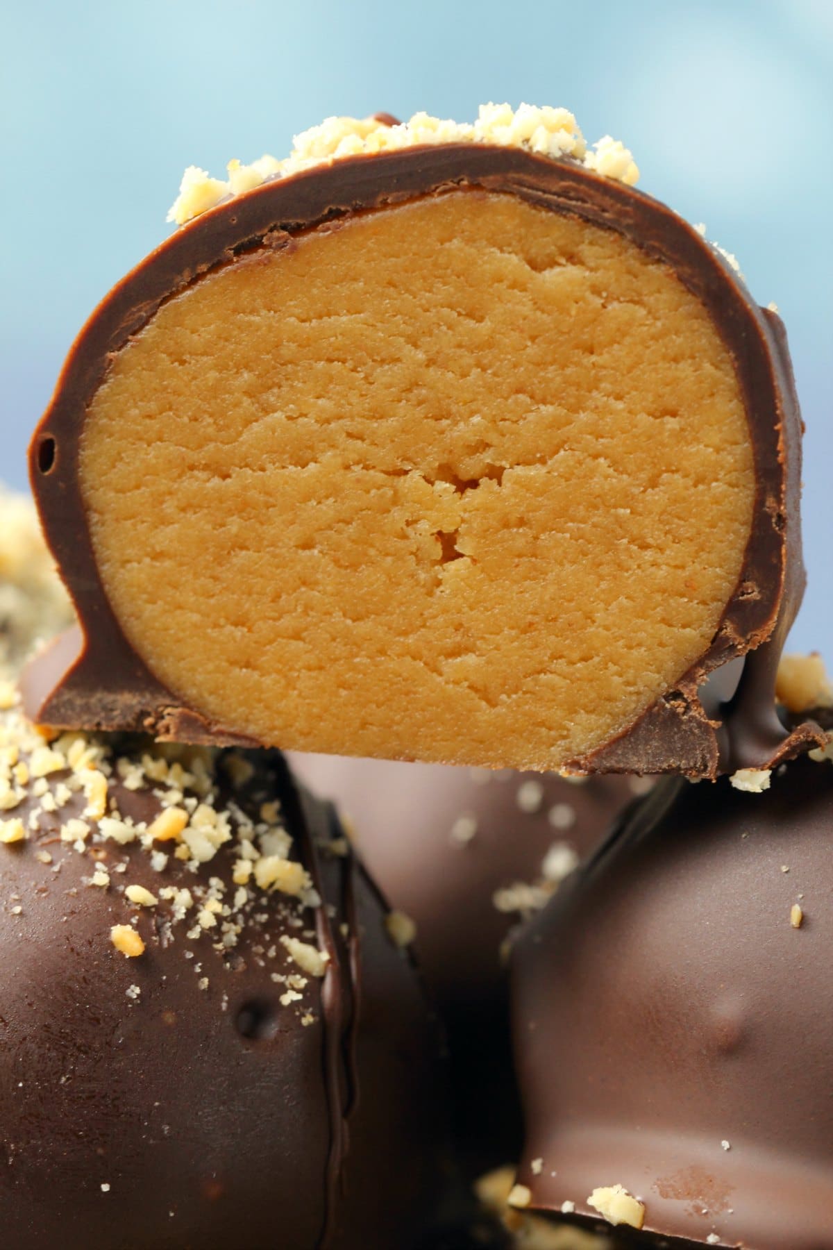 Vegan peanut butter balls stacked up with the top one cut in half to show the center. 