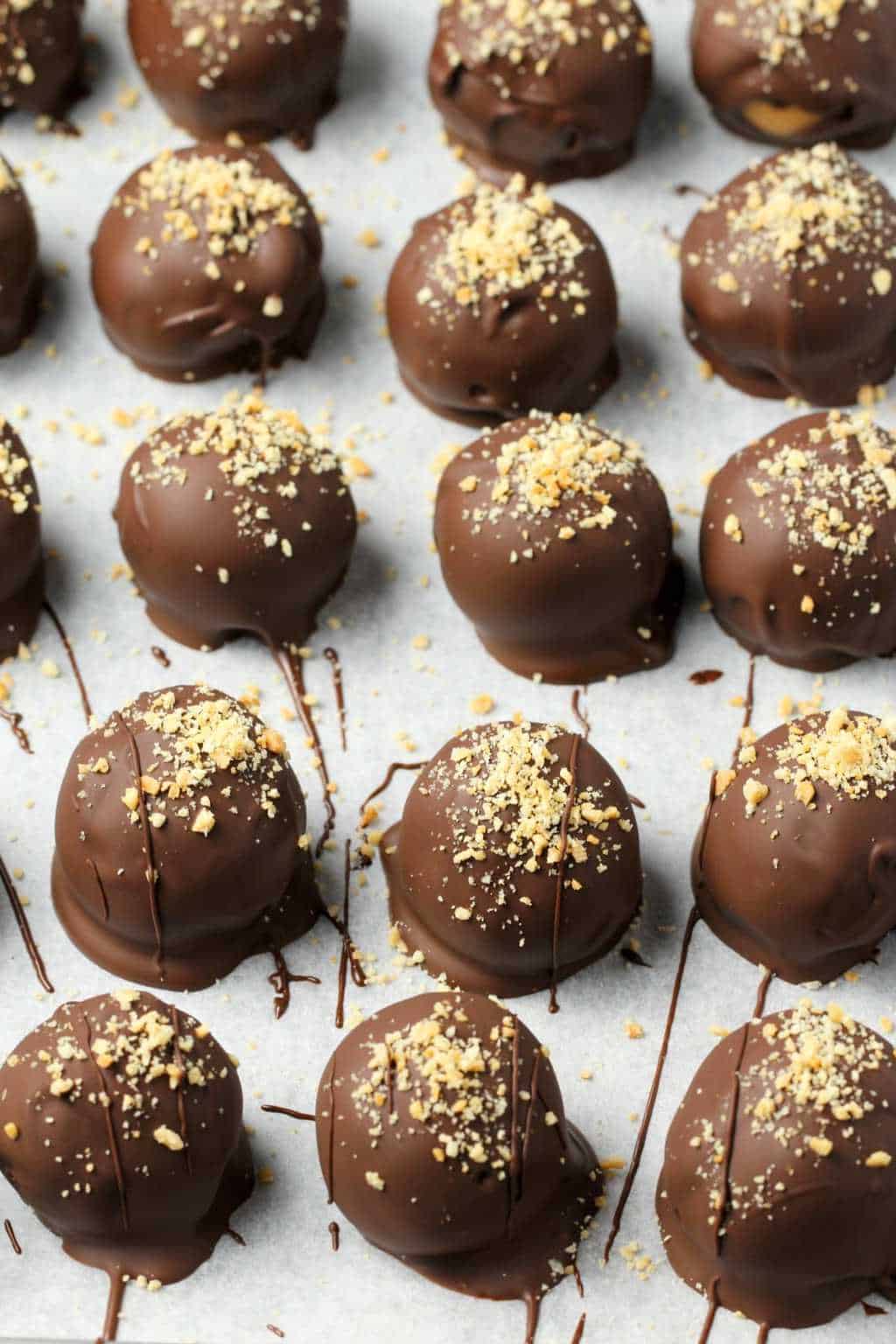 Vegan peanut butter balls smothered in chocolate on a parchment lined baking tray. 