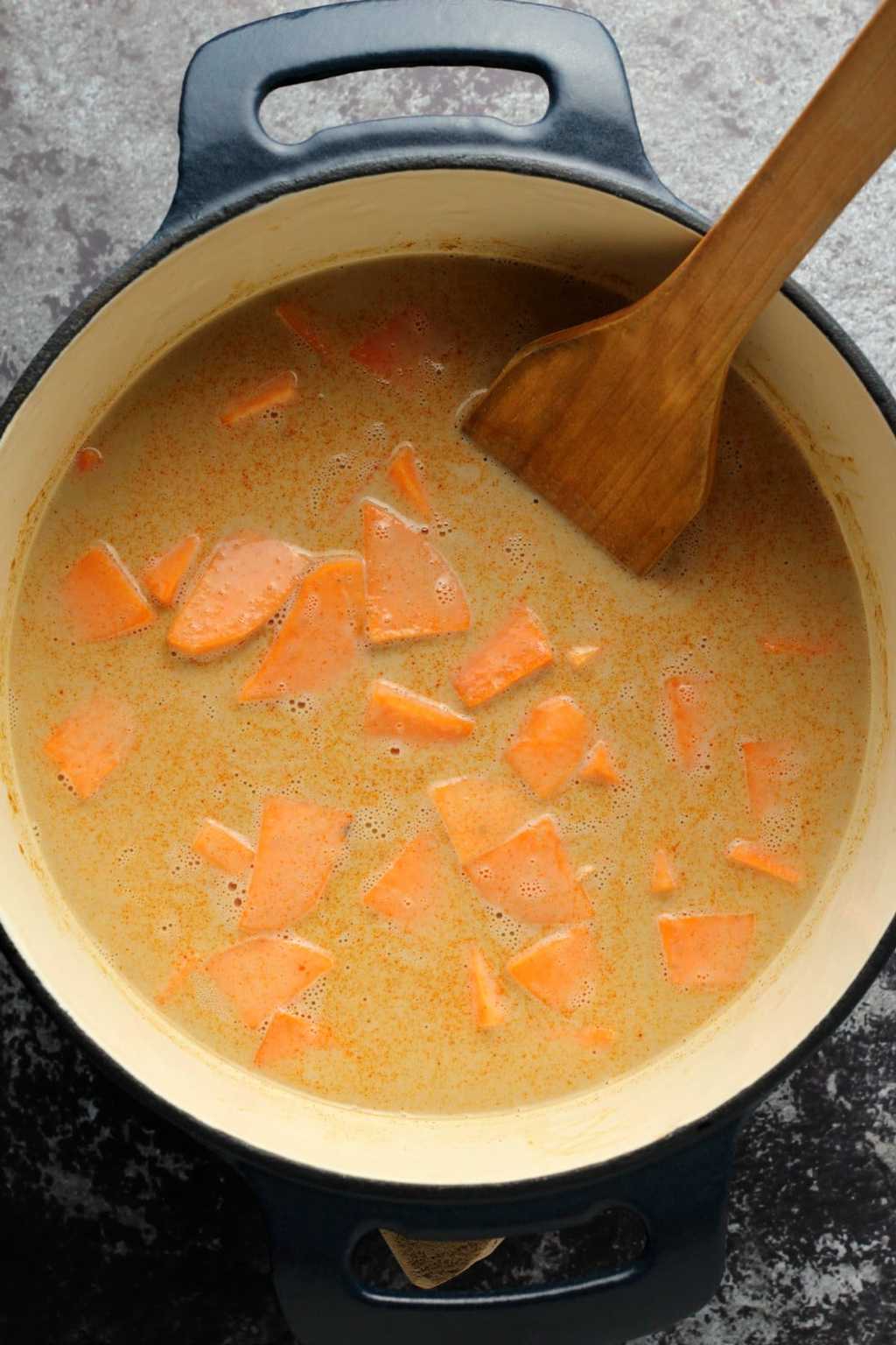 Sweet potato, coconut milk and spices in a cast iron pot with a wooden spoon.