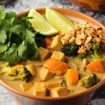 Vegan massaman curry with fresh lime and cilantro in a brown bowl.