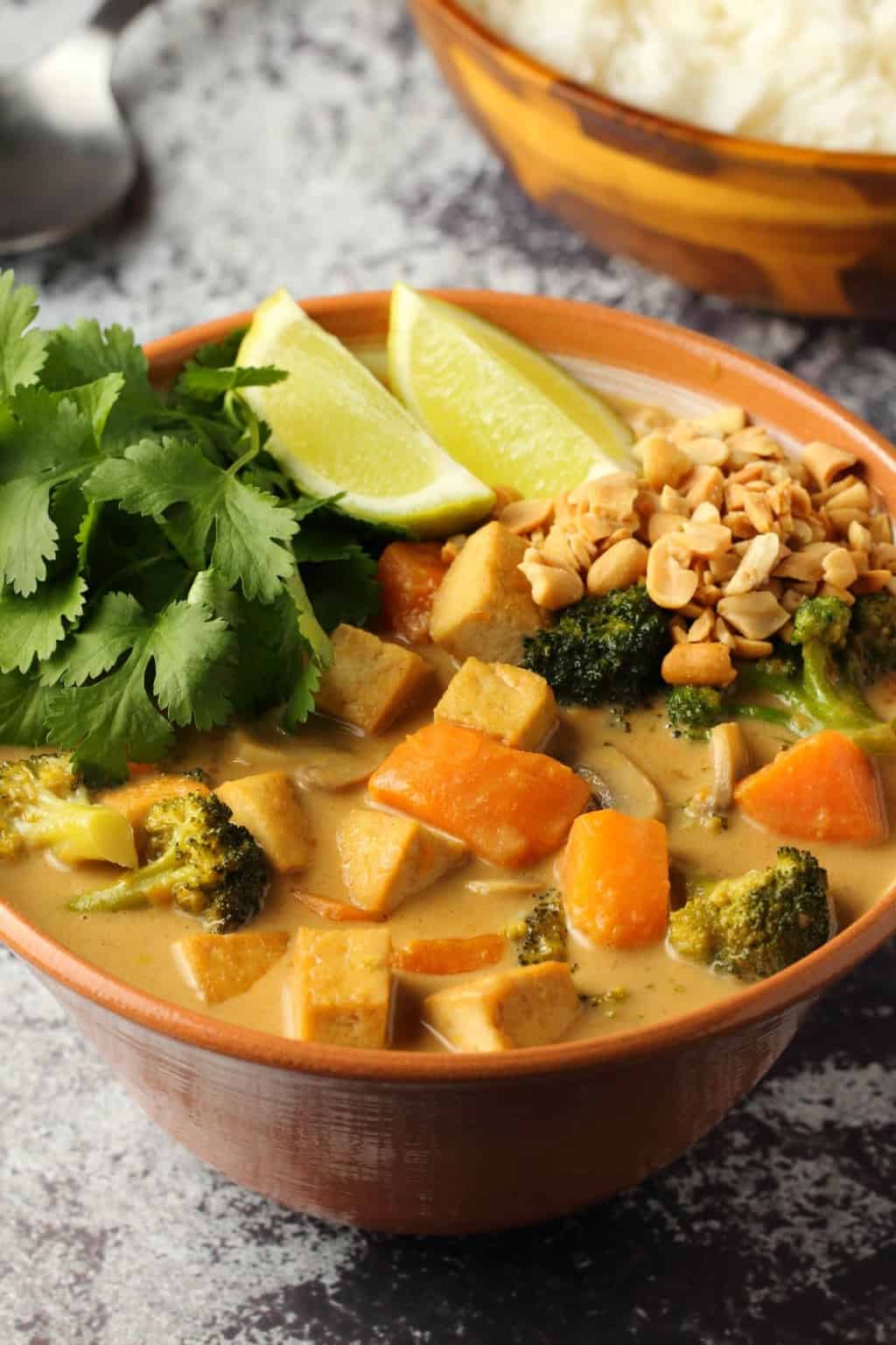 Vegan massaman curry in a bowl topped with crushed peanuts, fresh cilantro and wedges of lime. 
