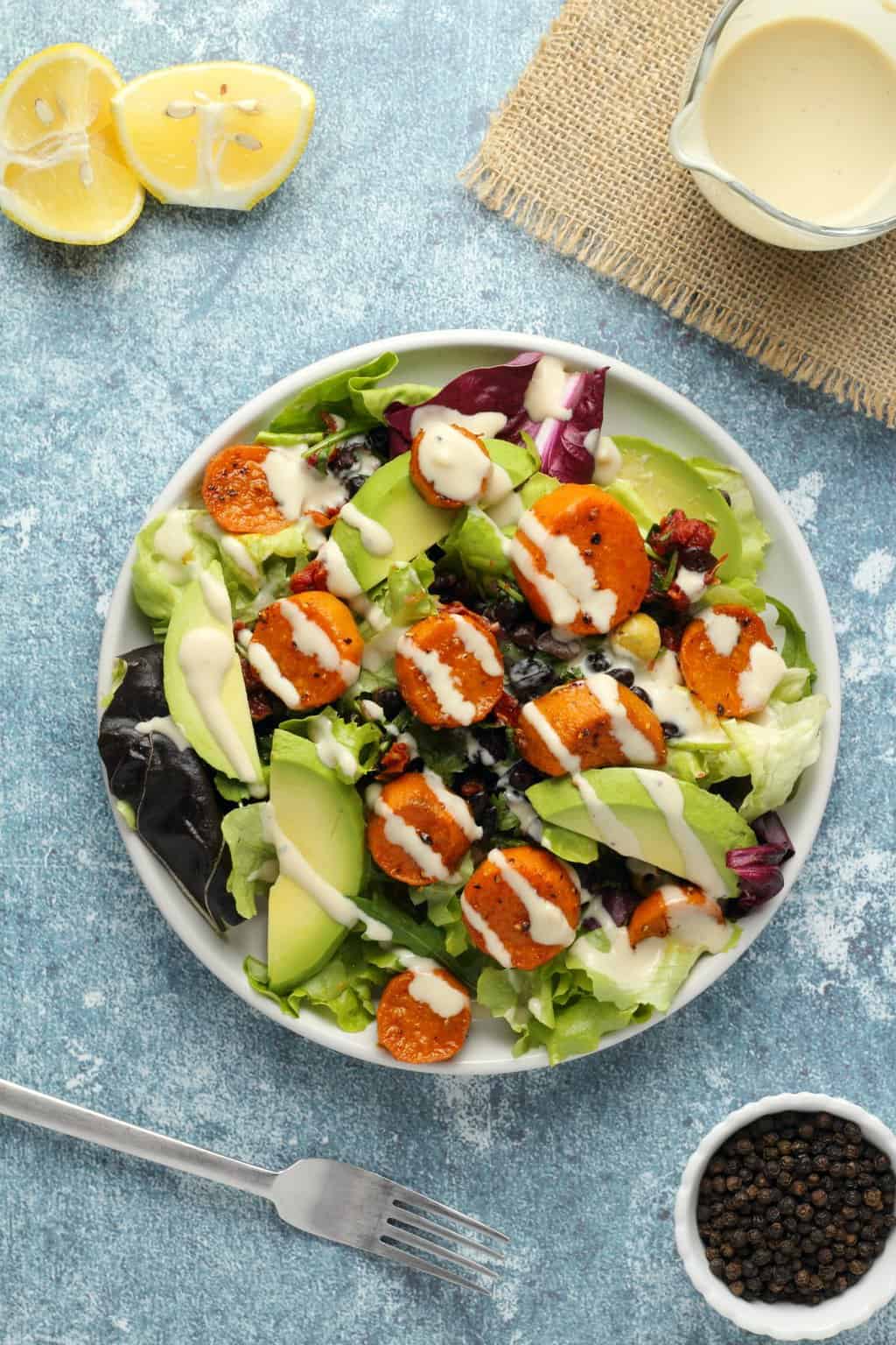 Vegan sweet potato salad topped with tahini dressing on a white plate. 