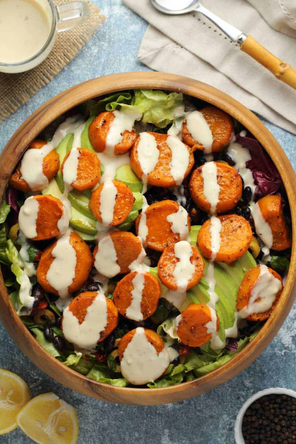 Vegan sweet potato salad topped with tahini dressing in a wooden salad bowl. 