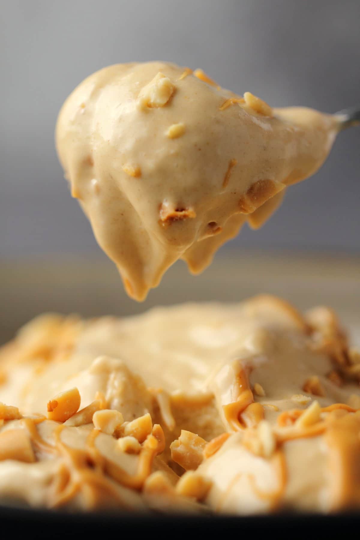 A spoonful of peanut butter nice cream lifting out of a bowl. 