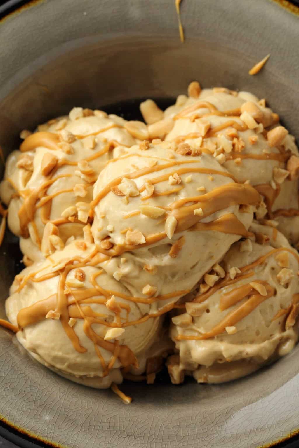 Banana Nice cream topped with drizzled peanut butter and crushed peanuts in a stone bowl. 
