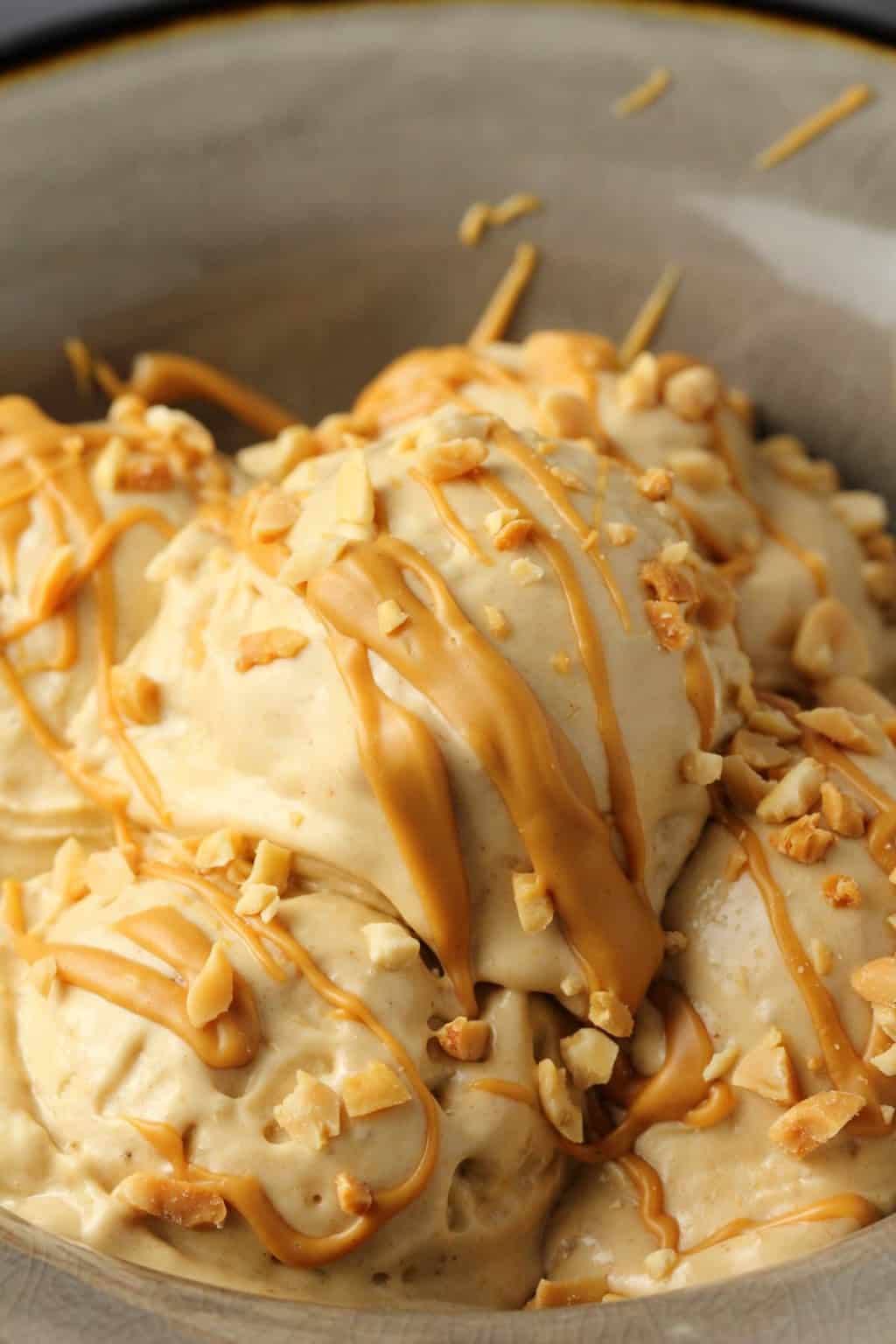 Peanut butter nice cream topped with drizzled peanut butter and crushed peanuts in a stone bowl. 