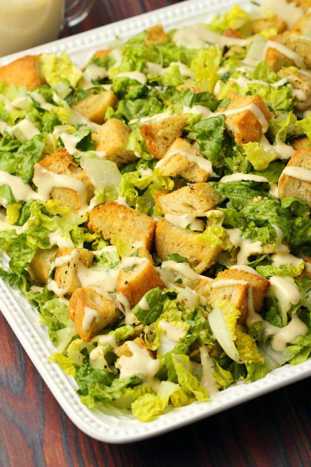 Vegan caesar salad topped with caesar dressing on a white salad platter. 