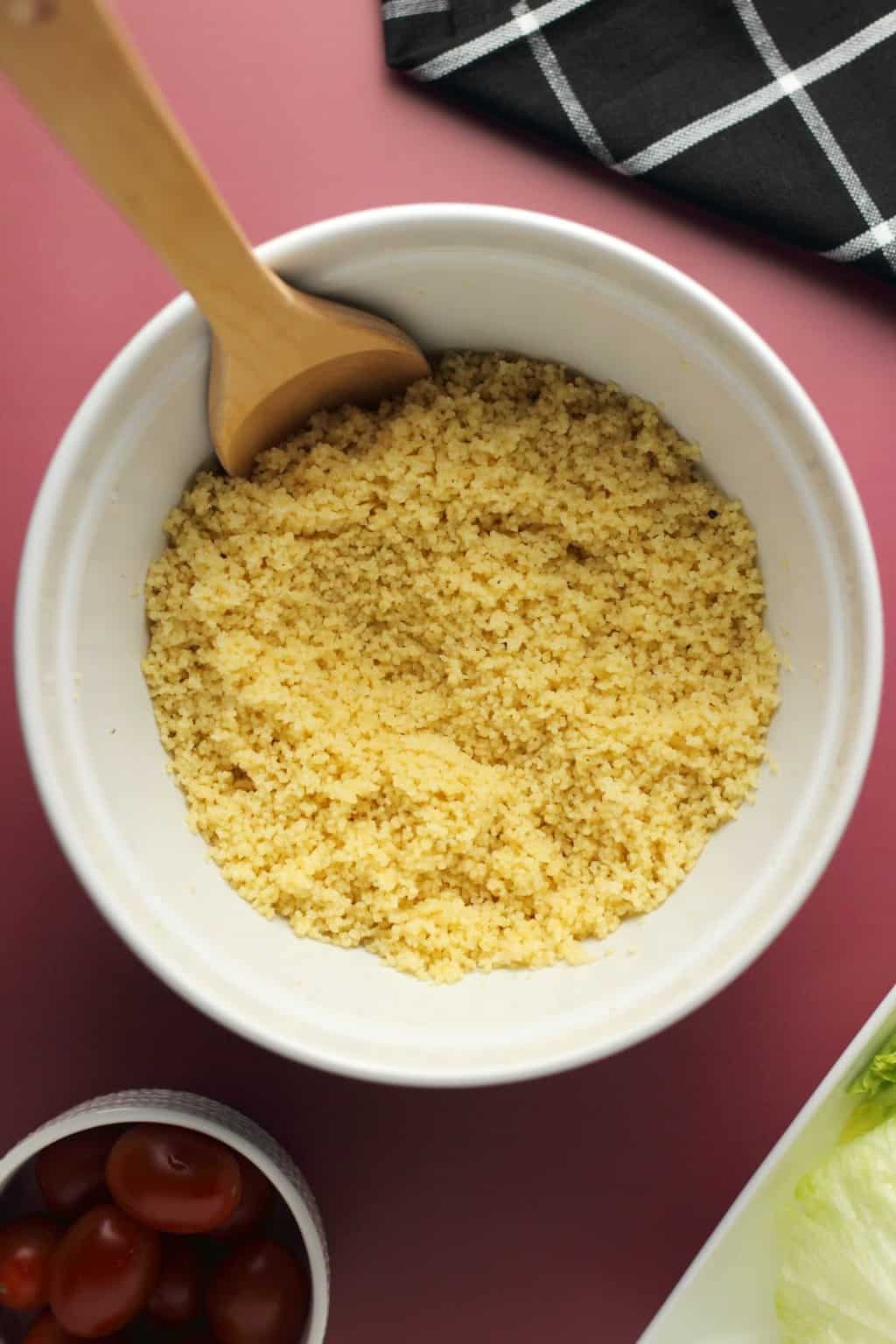 Couscous in a white bowl with a wooden spoon. 
