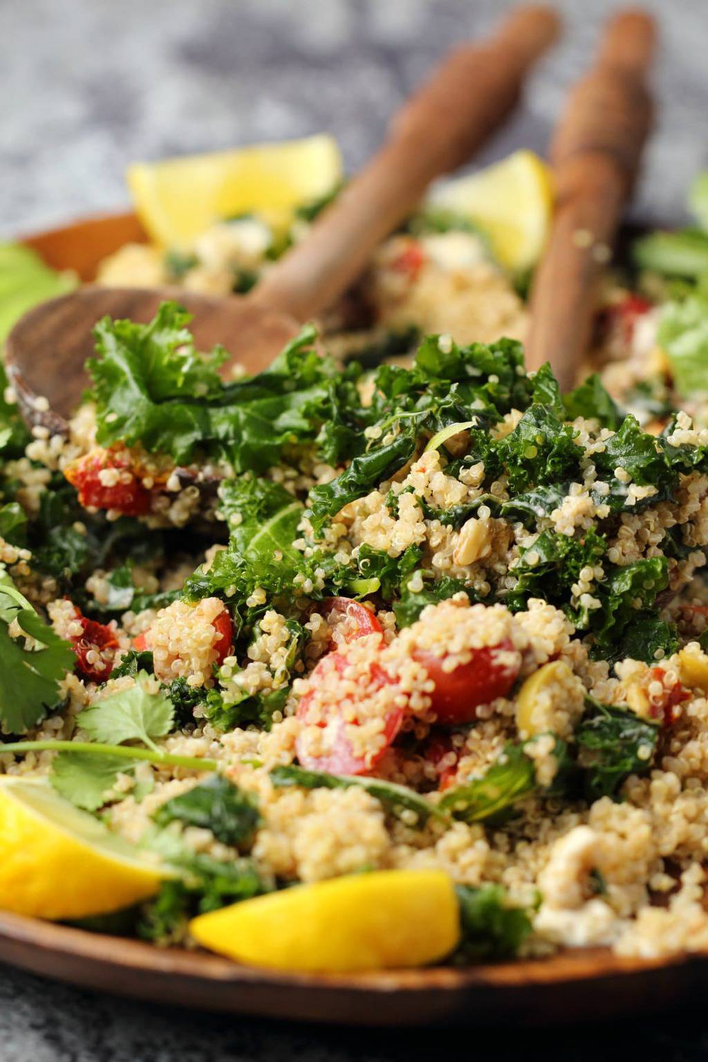 Vegan kale salad on a wooden salad platter with wooden salad spoons. 