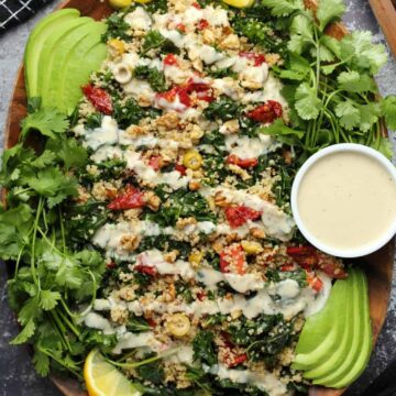Vegan kale salad topped with drizzled dressing on a wooden serving platter.