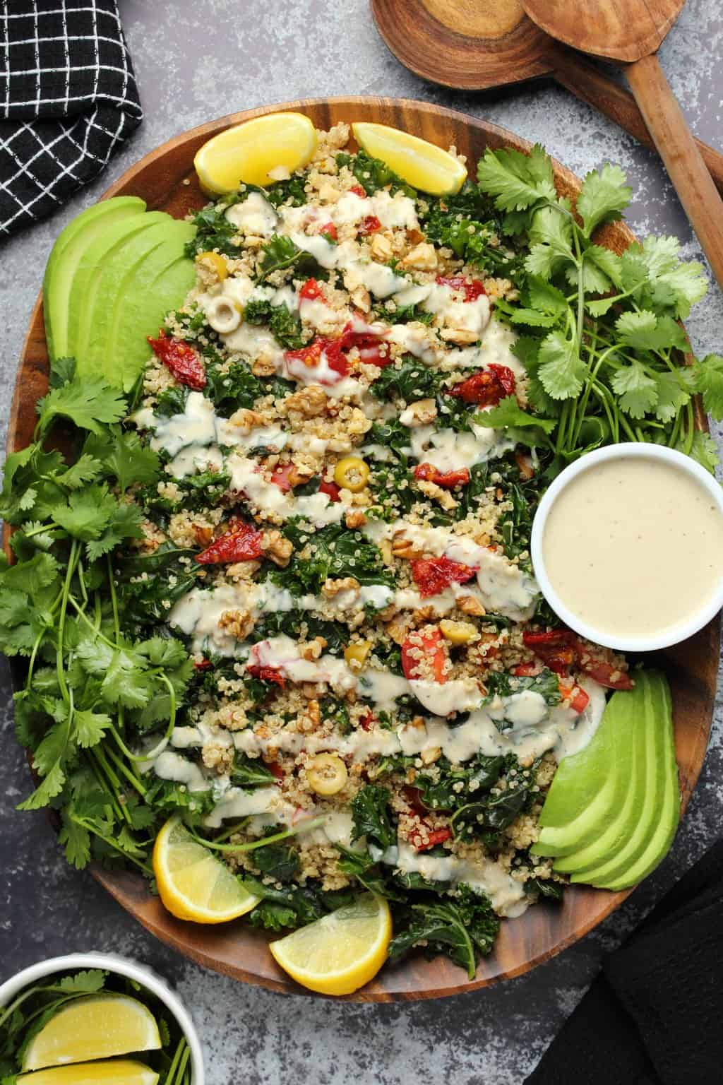 Vegan kale salad topped with tahini dressing on a wooden salad platter. 