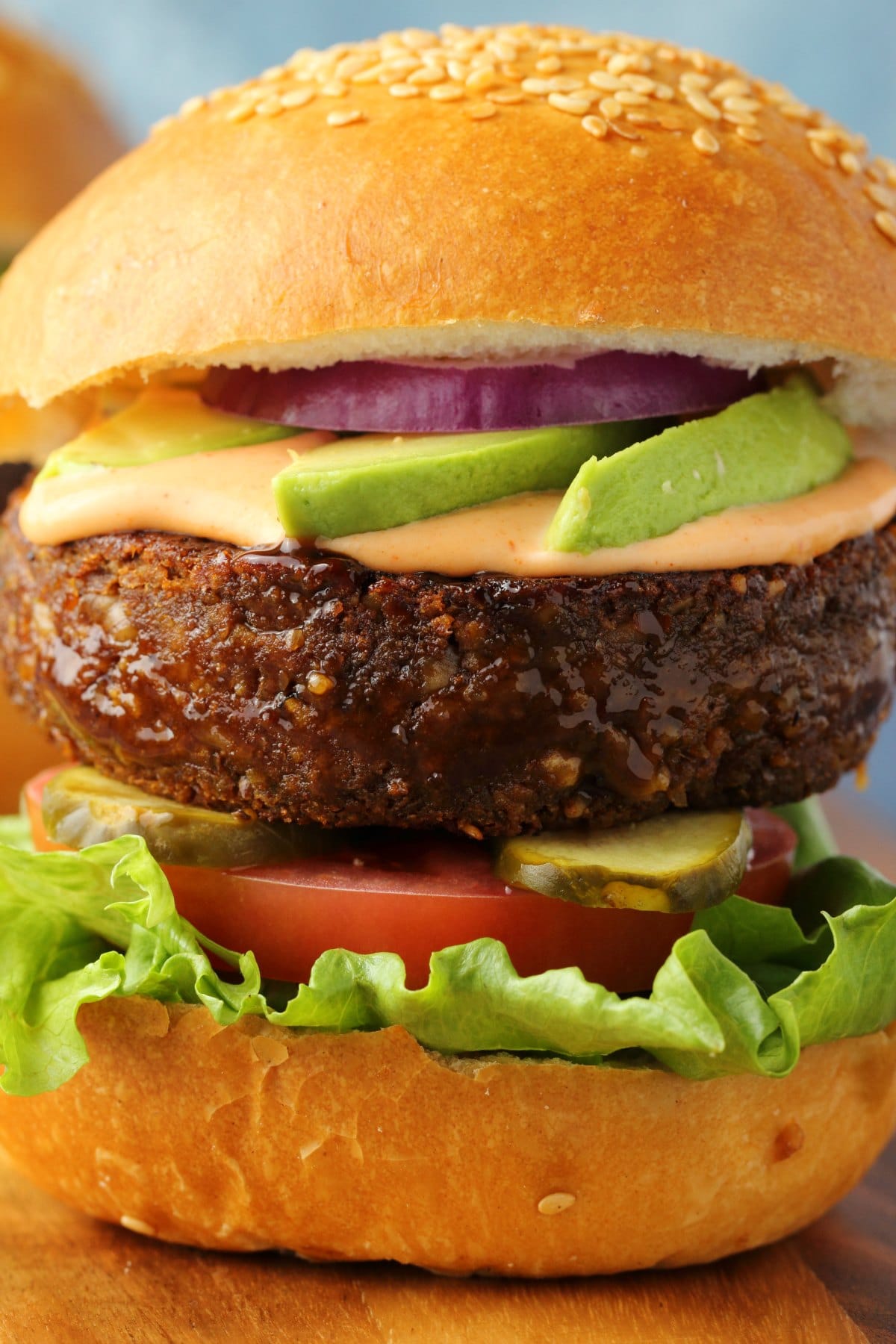 Vegan burger on a burger bun with lettuce, tomato, pickles, vegan thousand island, avocado and red onion. 