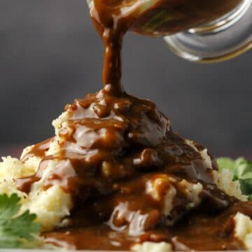 Vegan gravy pouring from a glass jug onto mashed potatoes