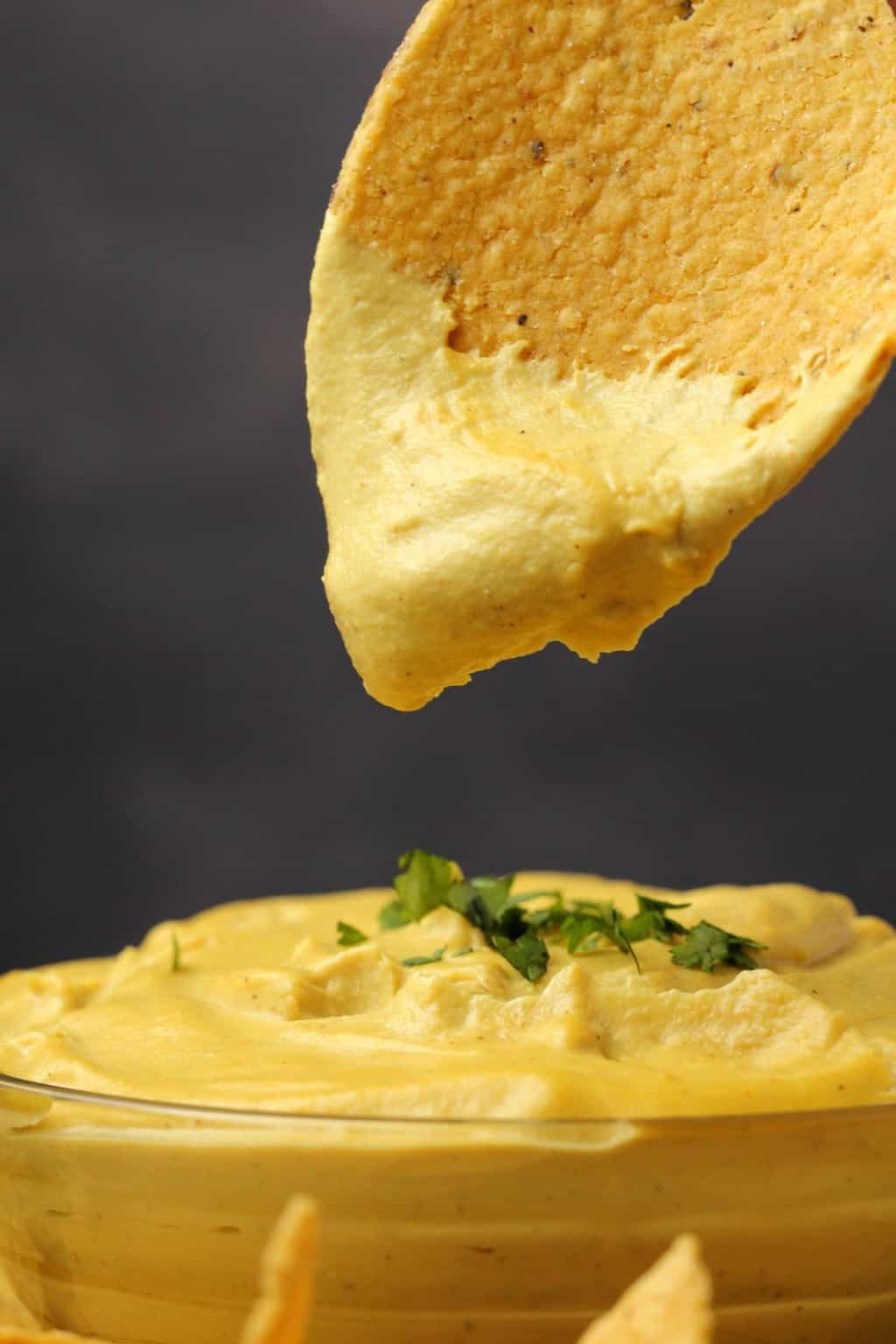 Vegan nacho cheese in a glass bowl with a freshly dipped tortilla chip above it. 